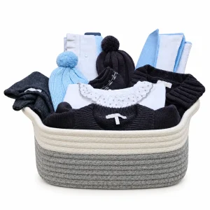 Cesta de nacimiento para bebé niño invierno con ropa de punto, gorros, manta, muselina y complementos presentada en cesta de tela reutilizable.